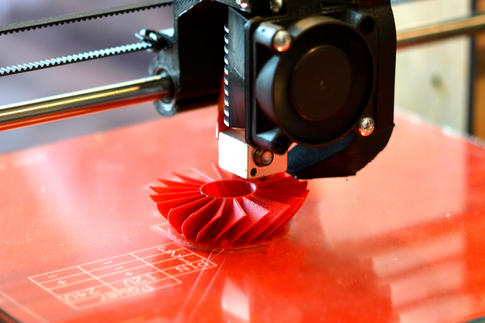 3D printer printing an orange fan-like component.