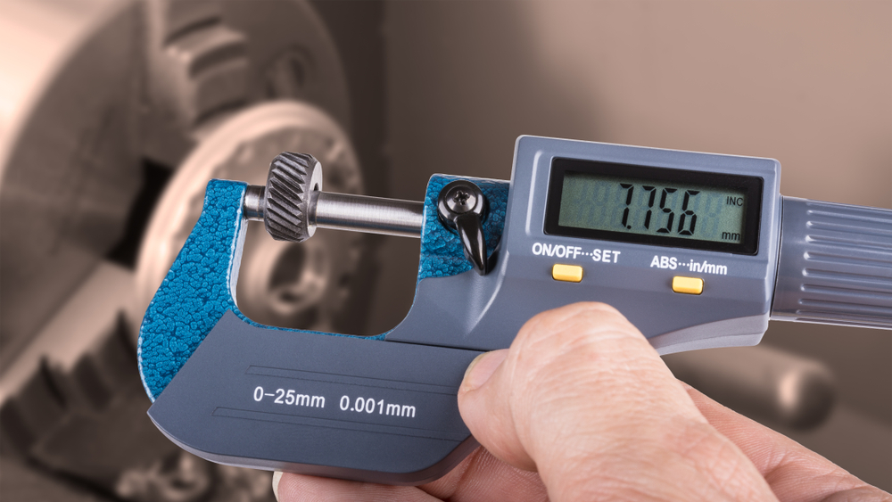 Person holding digital calipers and measuring a small gear.