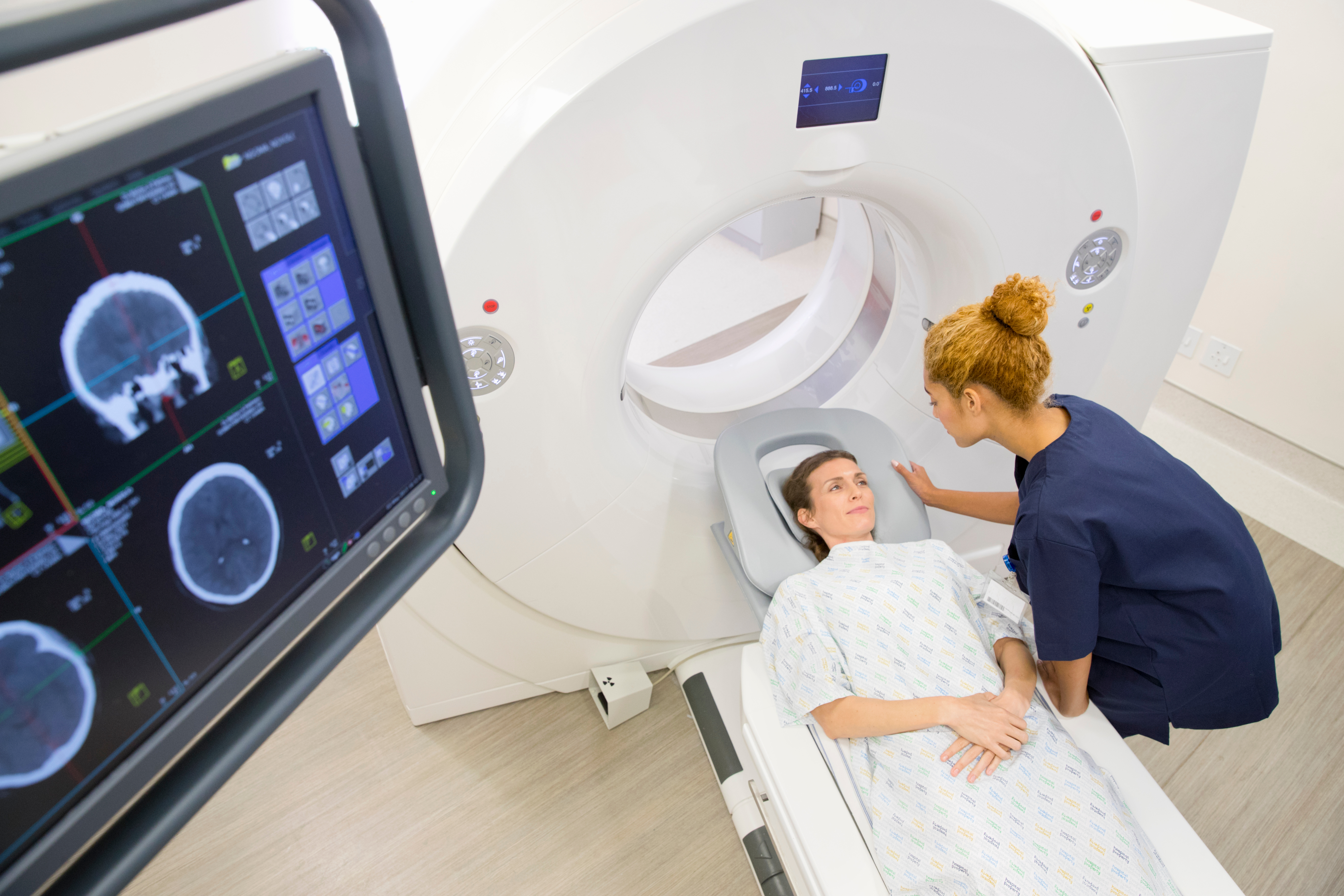 Female hospital radiographer with female patient operating CT scanner.