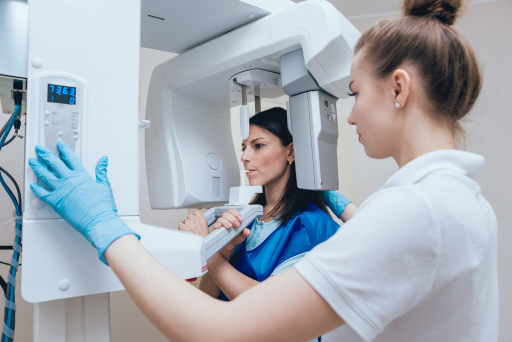 Young woman patient standing in X-ray machine. Panoramic radiography.